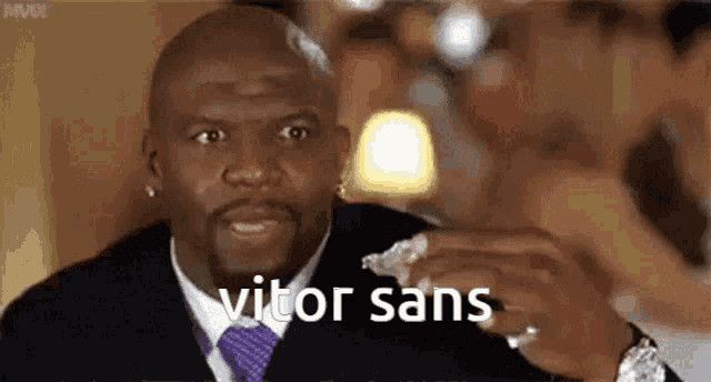 a man in a suit and tie is holding a piece of bread in his hand and says vitor sans .