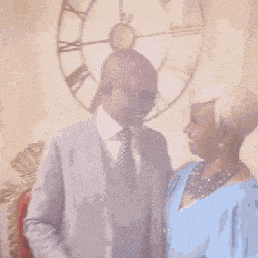 a man in a suit and tie is standing next to a woman in a blue dress in front of a large clock .