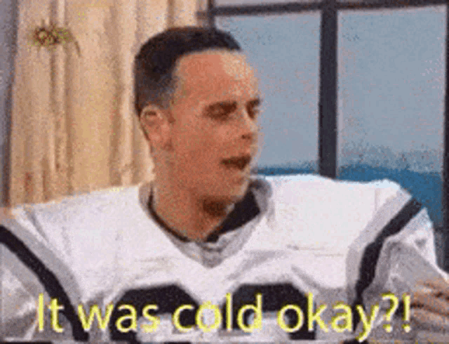 a man in a football uniform is sitting in front of a window and saying it was cold okay .