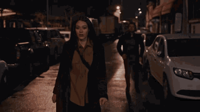 a woman walking down a street at night with a man behind her