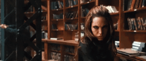 a woman is standing in front of a bookshelf in a library holding a sword .