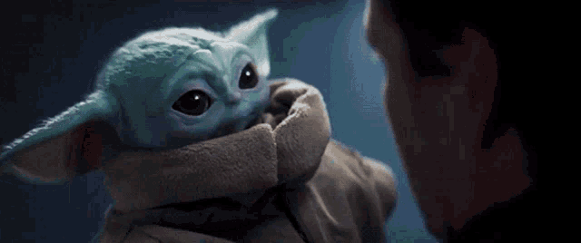 a man is holding a stuffed animal that looks like the child from star wars .