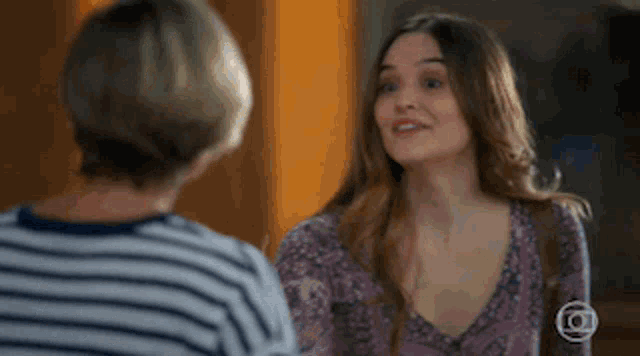 a woman in a striped shirt is talking to another woman in a purple top