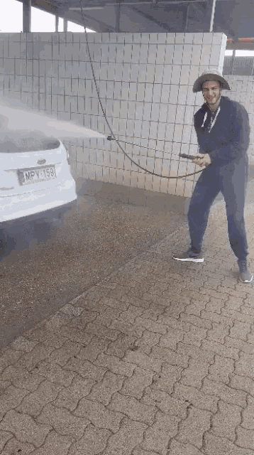 a man in a cowboy hat is spraying a car with a high pressure washer