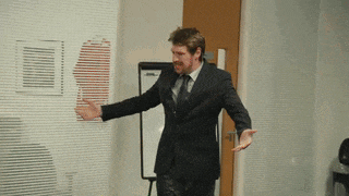 a man in a suit and tie is dancing in front of a white board