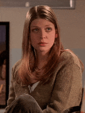 a woman wearing a sweater and earrings sits in front of a framed picture