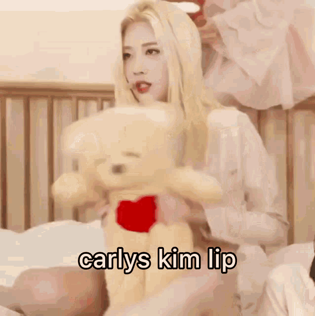 a woman with blonde hair is holding a teddy bear with a heart on it and the words carlys kim lip written below her