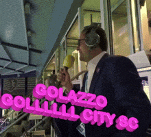 a man wearing headphones holds a microphone in front of a sign that says golazzo