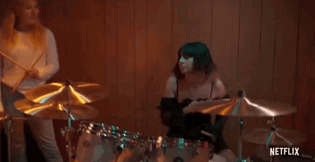 a woman is playing drums in a dark room while another woman watches .