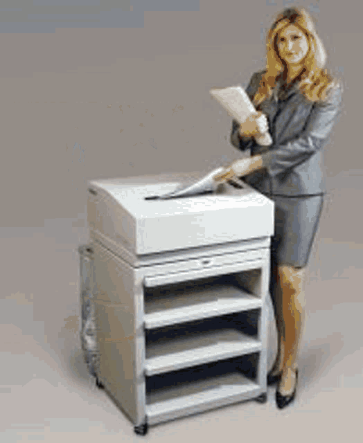 a woman in a business suit is standing next to a paper shredder .