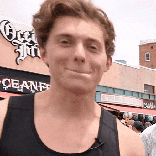 a man wearing a black tank top smiles in front of a sign that says ocean