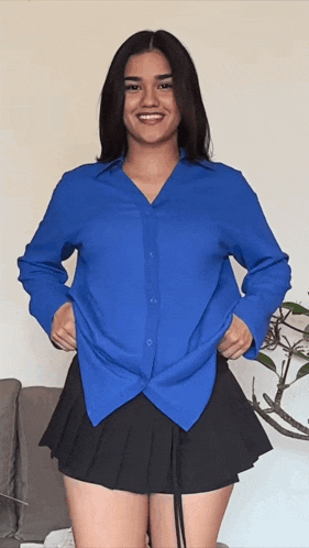 a woman in a blue shirt and black skirt smiles
