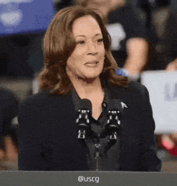 a woman speaking into a microphone with uscg written on the screen behind her