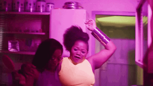 a woman in a yellow tank top is dancing with another woman in a kitchen .