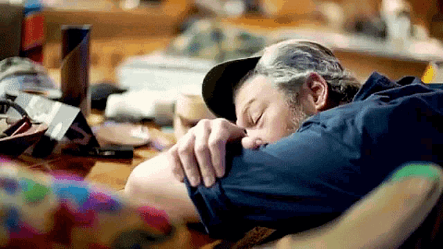 a man wearing a hat is sleeping in front of a laptop