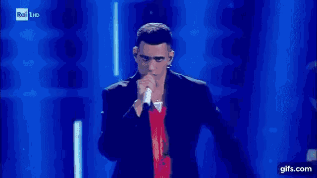 a man in a suit and red shirt is singing into a microphone on stage .