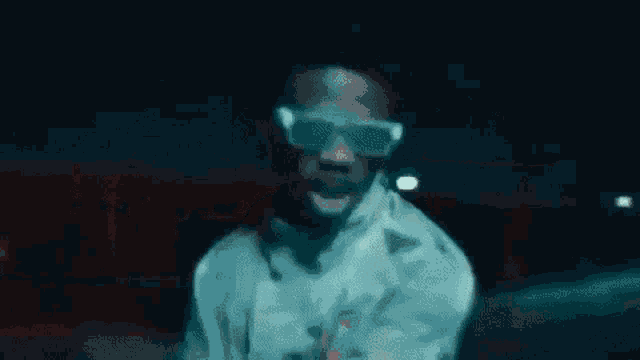 a man wearing sunglasses is standing in a dark room .
