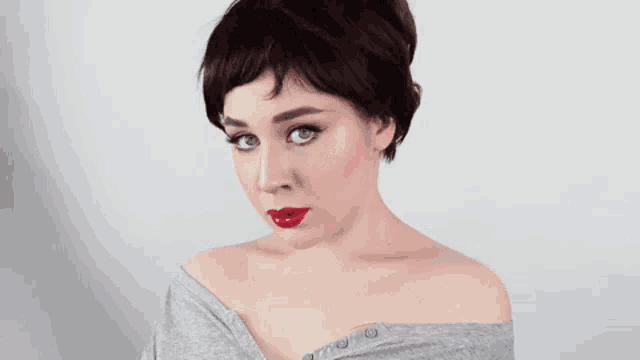 a woman with short hair and red lipstick is wearing a gray shirt .