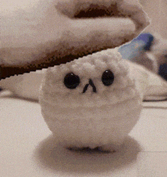 a white stuffed animal with black eyes is sitting on a white table