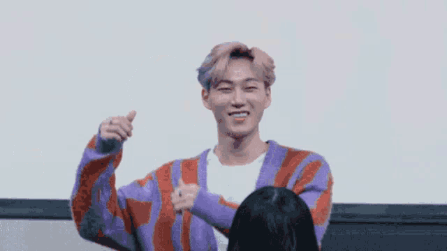 a man in a purple and red sweater is giving a thumbs up sign .