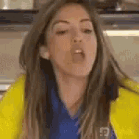 a woman is wearing a yellow jacket and a blue shirt and making a funny face .