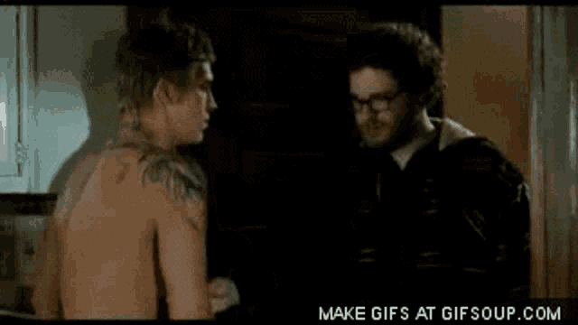 two shirtless men are standing next to each other and one has a tattoo on his shoulder .