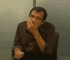 a man is sitting at a table smoking a cigarette and covering his mouth .