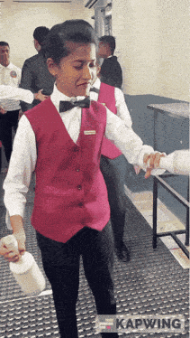 a girl wearing a red vest and a bow tie is holding a cup
