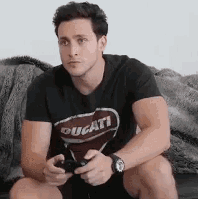 a man is sitting on a couch playing a video game while wearing a ducati t-shirt .