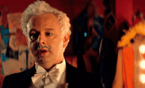 a man in a tuxedo and bow tie has a fake mustache painted on his face .