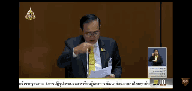 a man in a suit and tie is speaking into a microphone in front of a sign language sign