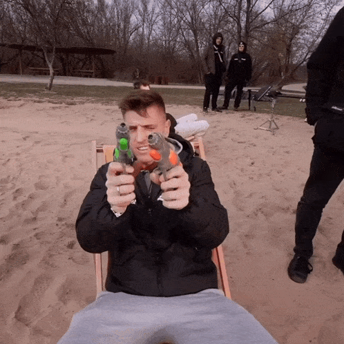 a man in a black jacket is sitting in a chair holding two water guns