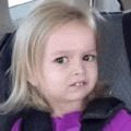 a little girl is sitting in a car seat wearing a purple shirt and a black vest .