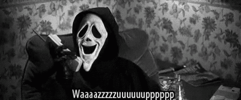 a person wearing a scream mask is sitting on a couch and talking on a cell phone .