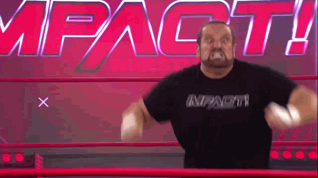a man wearing a black shirt that says impact is standing in a wrestling ring