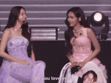 two women are sitting next to each other on a stage and one of them says do you love me