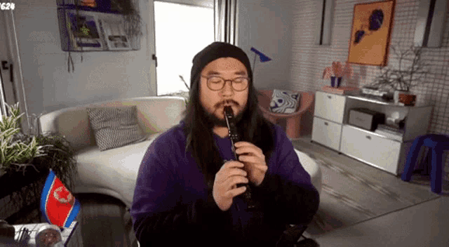 a man in a purple shirt is playing a flute in front of a couch