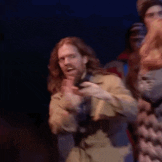 a man with long hair and a beard is standing on a stage holding a cell phone .