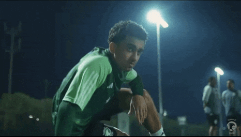 a young man in a green soccer uniform is sitting on the ground .