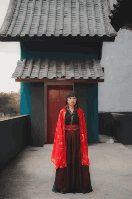 a woman in a red and black kimono stands in front of a building