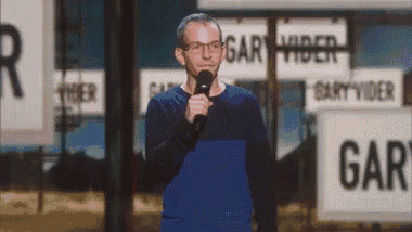 a man in a blue shirt is holding a microphone in front of a sign that says garry .