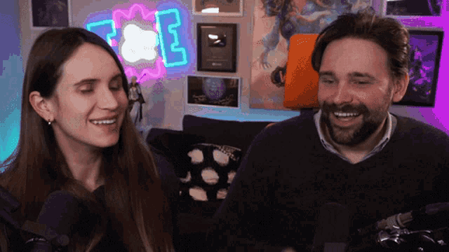 a man and a woman are smiling in front of a neon sign that says z & e on it