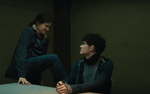 a woman in a black jacket is kneeling on a table with another woman