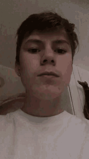 a young man wearing a white shirt is taking a selfie with his phone .