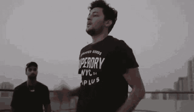 two men are standing next to each other on a balcony . one of the men is wearing a superdry t-shirt .