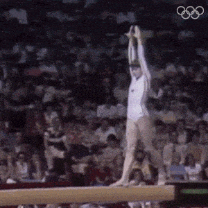 a female gymnast is doing a trick on a balance beam while a crowd watches .