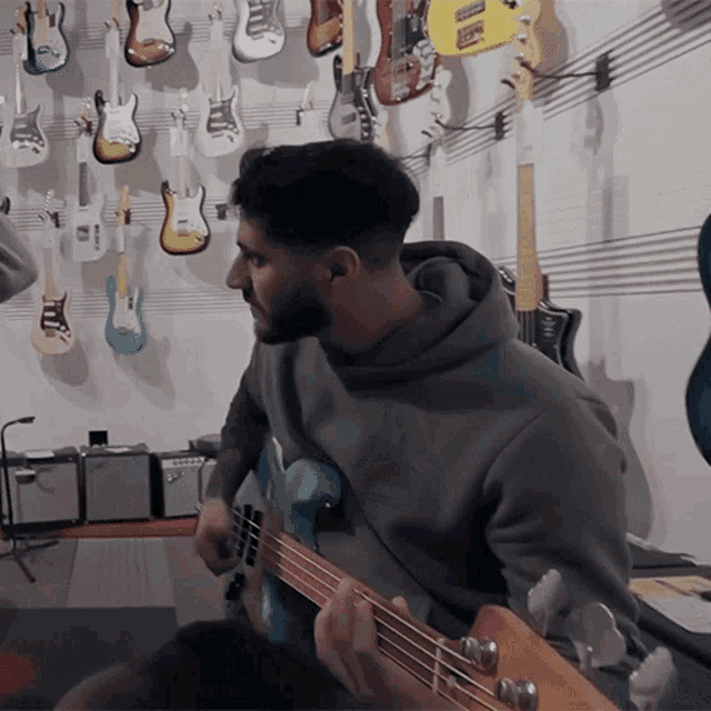 a man plays a guitar in front of a wall of guitars