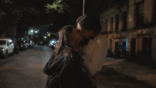 a man and a woman are kissing on the street at night
