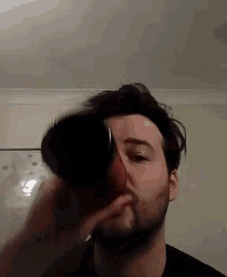 a man with a beard is drinking from a glass in a living room .