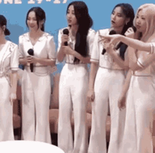 a group of women are standing next to each other holding microphones and singing into them .